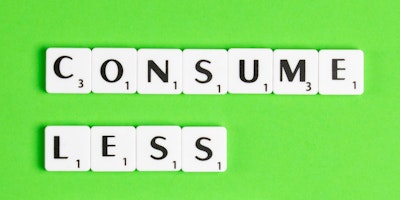 Scrabble letter pieces spell out the message 'consume less' against a green background