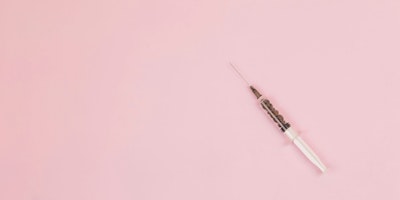 A syringe against a pink background