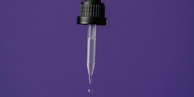 A hand squeezes a drop of liquid from a pipette 