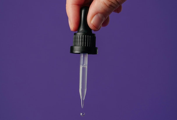 A hand squeezes a drop of liquid from a pipette 