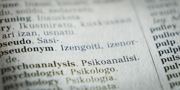 A close-up photograph of a page in the dictionary focuses on the word 'pseudonym'