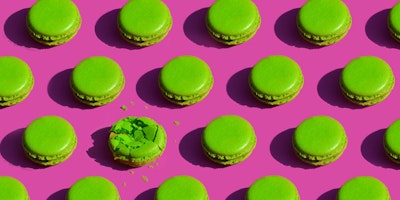 Green macarons on a pink background. One of them is smashed