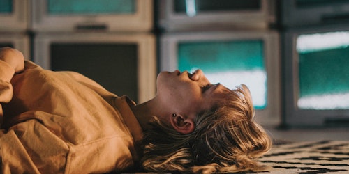 Girl lying on floor surrounded by TVs