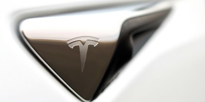 A white Tesla logo on a silver-coloured handle against a white background