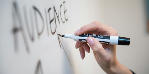 A hand holds a black marker pen over a whiteboard on which the word 'audience' is written with arrows pointing towards it