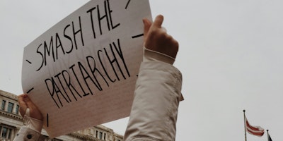 Two hands hold up a sign that reads 'smash the patriarchy' 