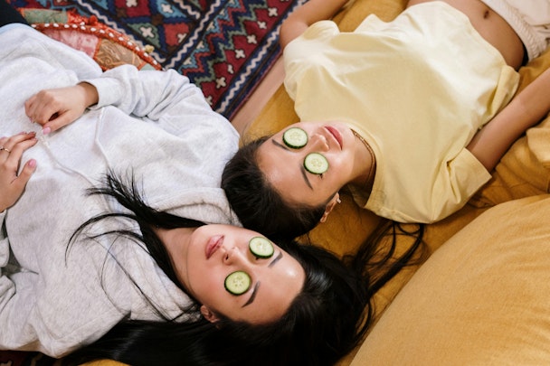 Two girls wearing cucumbers on their faces 