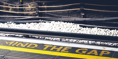 A photograph of a sign written on a London underground station platform reading 'mind the gap'