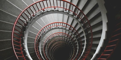 A photo taken down the middle of a concrete spiral staircase with a red handrail