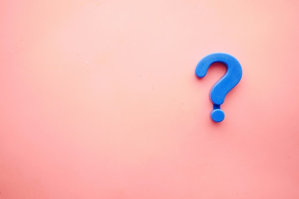 A blue plastic question mark against a pink background