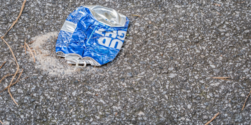 Crushed Bud Light beer can flattened on black asphalt